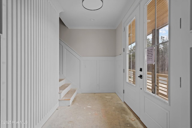 doorway featuring a decorative wall, unfinished concrete flooring, and a wainscoted wall