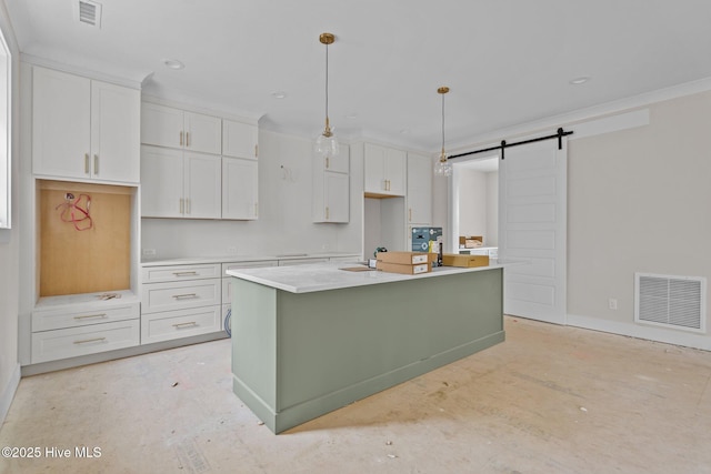 kitchen with a barn door, visible vents, white cabinets, and an island with sink