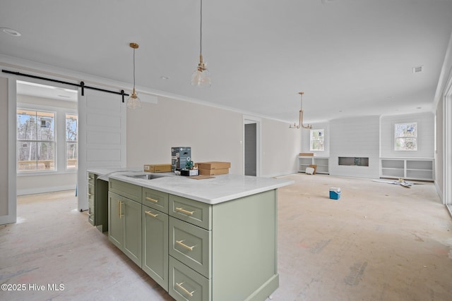 kitchen featuring a barn door, green cabinetry, decorative light fixtures, light countertops, and a sink