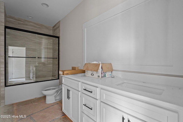 full bath with toilet, double vanity, a sink, and bath / shower combo with glass door
