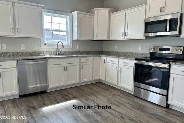 kitchen with light stone countertops, stainless steel appliances, dark wood-type flooring, sink, and white cabinetry