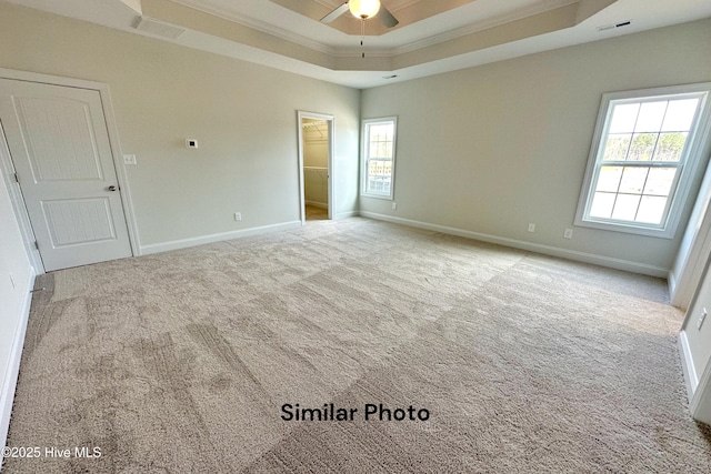 empty room featuring light carpet, a raised ceiling, ceiling fan, and ornamental molding