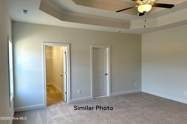 unfurnished bedroom with a tray ceiling, a spacious closet, light colored carpet, and ornamental molding