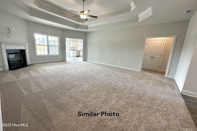 unfurnished living room with a raised ceiling, ceiling fan, crown molding, and carpet floors