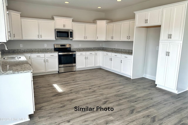 kitchen with light stone countertops, sink, dark hardwood / wood-style floors, white cabinets, and appliances with stainless steel finishes