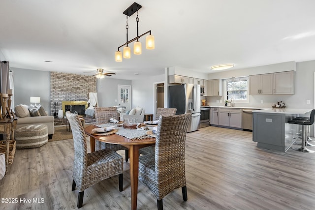 dining room with light hardwood / wood-style floors, ceiling fan, a brick fireplace, and sink