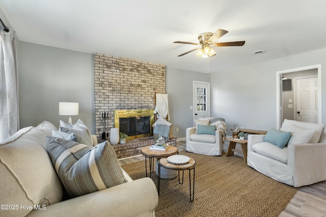 living room with ceiling fan, a brick fireplace, and wood-type flooring