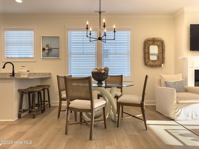 dining space with light hardwood / wood-style floors, sink, ornamental molding, and a notable chandelier