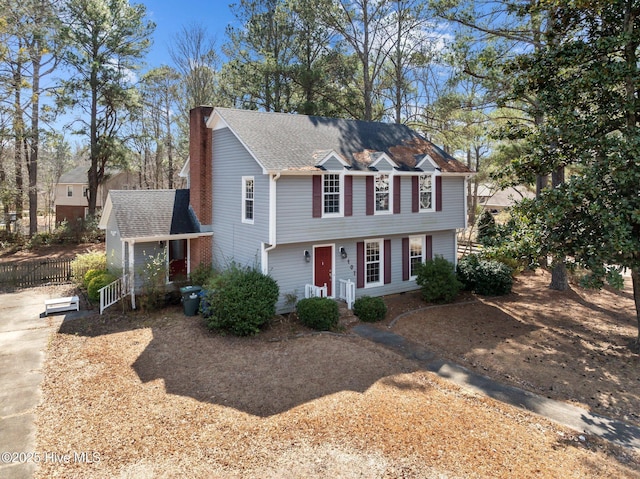 colonial house with roof with shingles, a chimney, fence, and driveway