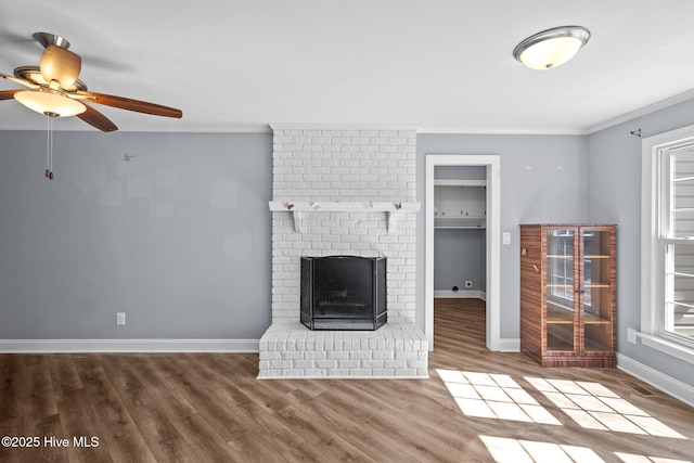 unfurnished living room featuring baseboards, ornamental molding, wood finished floors, a brick fireplace, and a wealth of natural light