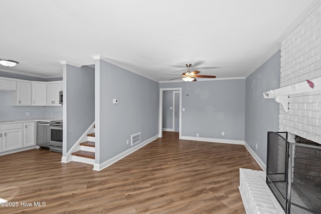 unfurnished living room featuring ceiling fan, visible vents, a brick fireplace, dark wood-style floors, and crown molding