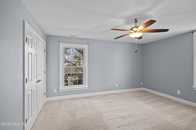 carpeted empty room featuring visible vents, a ceiling fan, and baseboards