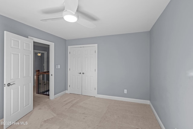 unfurnished bedroom with baseboards, ceiling fan, a closet, and light colored carpet