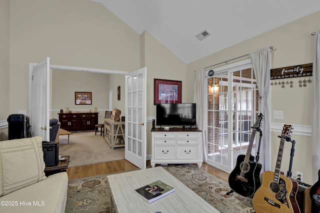 living room featuring lofted ceiling, light wood-type flooring, and french doors