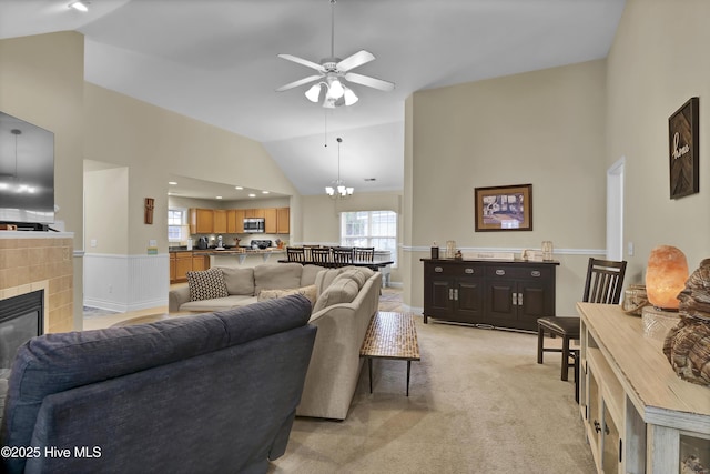 tiled living room with vaulted ceiling, ceiling fan with notable chandelier, and a tiled fireplace