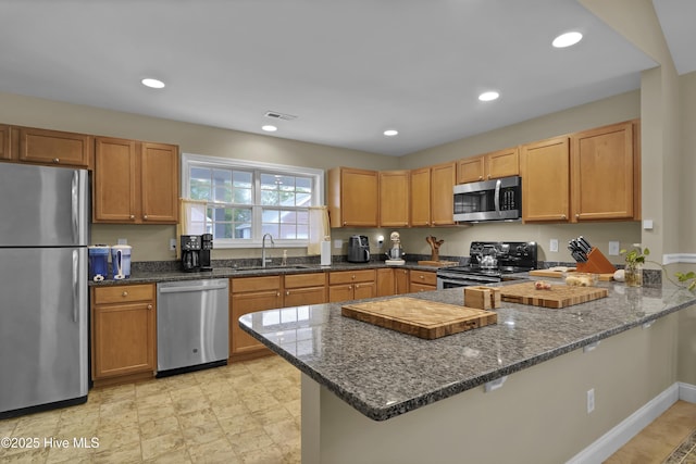 kitchen with stainless steel appliances, kitchen peninsula, dark stone counters, and sink