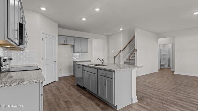 kitchen with backsplash, gray cabinets, a kitchen island with sink, and sink