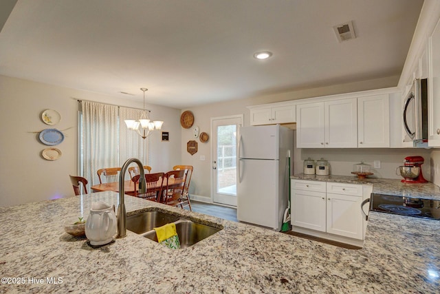 kitchen with white fridge, white cabinets, light stone countertops, and a chandelier