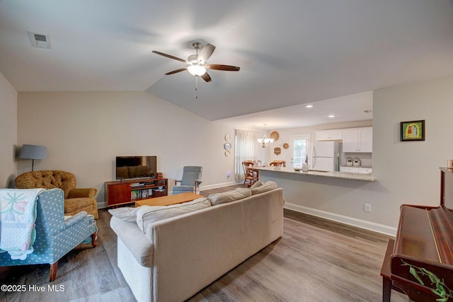 living room with ceiling fan with notable chandelier, vaulted ceiling, and light hardwood / wood-style flooring