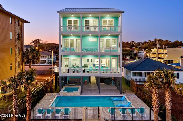 back house at dusk featuring a pool with hot tub, a balcony, and a patio