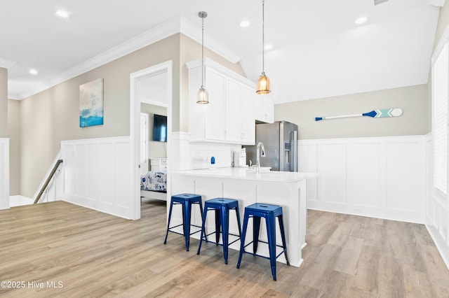 kitchen with white cabinetry, stainless steel refrigerator with ice dispenser, a kitchen island with sink, ornamental molding, and pendant lighting