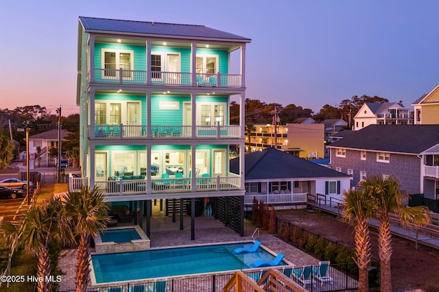 back house at dusk with a swimming pool with hot tub, a balcony, and a patio