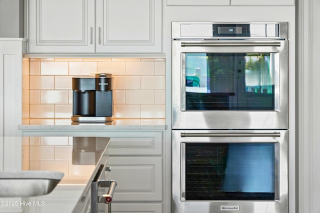 kitchen with decorative backsplash, light stone counters, white cabinets, and double oven