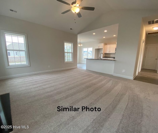 unfurnished living room with light carpet, ceiling fan with notable chandelier, vaulted ceiling, and sink