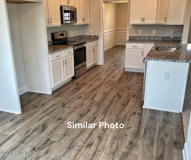 kitchen featuring sink, dark hardwood / wood-style flooring, dark stone counters, white cabinets, and appliances with stainless steel finishes