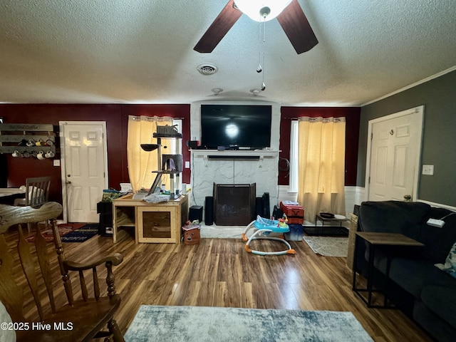 living room featuring a textured ceiling, ceiling fan, crown molding, hardwood / wood-style flooring, and a fireplace