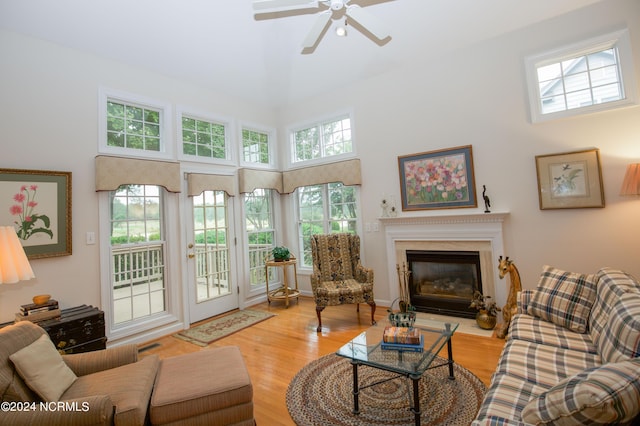 living room featuring a towering ceiling, light wood-type flooring, ceiling fan, and a wealth of natural light