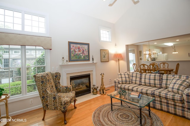 living room with ceiling fan with notable chandelier, a high end fireplace, high vaulted ceiling, and wood-type flooring