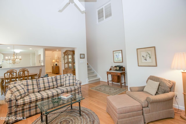 living room with a high ceiling, light hardwood / wood-style floors, and ceiling fan with notable chandelier