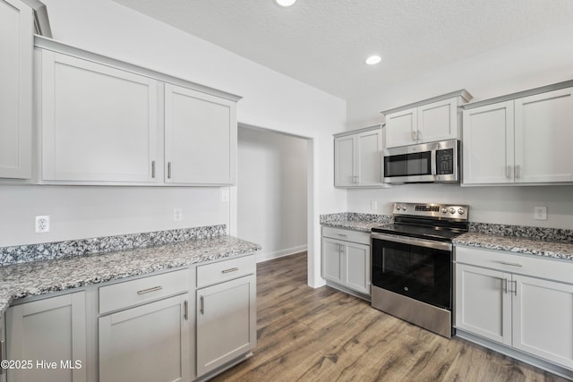 kitchen featuring hardwood / wood-style floors, stainless steel appliances, a textured ceiling, and light stone countertops