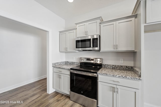 kitchen featuring vaulted ceiling, light hardwood / wood-style flooring, a textured ceiling, appliances with stainless steel finishes, and light stone countertops