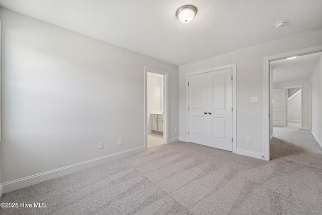 unfurnished bedroom with ensuite bath, light colored carpet, a textured ceiling, and a closet