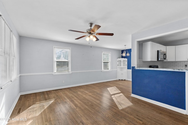 unfurnished living room featuring ceiling fan with notable chandelier and dark hardwood / wood-style flooring