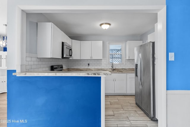 kitchen featuring kitchen peninsula, stainless steel appliances, backsplash, white cabinets, and sink