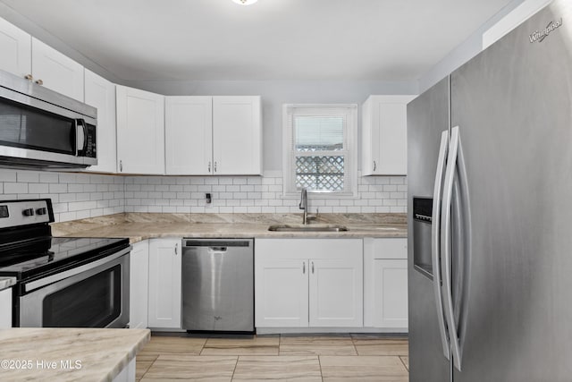 kitchen featuring tasteful backsplash, sink, white cabinetry, appliances with stainless steel finishes, and light stone counters