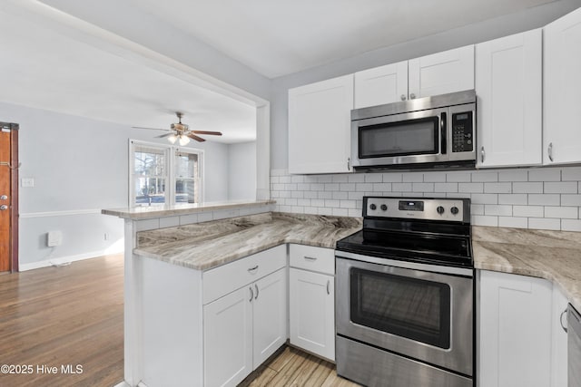 kitchen featuring kitchen peninsula, decorative backsplash, stainless steel appliances, and white cabinetry