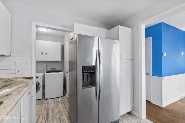 kitchen featuring white cabinets, washing machine and dryer, stainless steel fridge with ice dispenser, and light stone counters