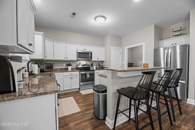 kitchen featuring a breakfast bar, dark wood-type flooring, white cabinets, sink, and appliances with stainless steel finishes