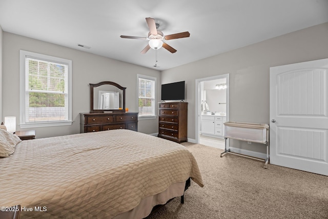 bedroom with connected bathroom, ceiling fan, light colored carpet, and multiple windows