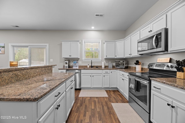 kitchen with sink, dark hardwood / wood-style floors, dark stone countertops, white cabinetry, and stainless steel appliances