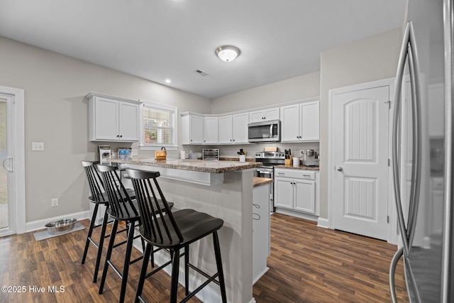 kitchen featuring dark hardwood / wood-style flooring, white cabinetry, a breakfast bar area, and appliances with stainless steel finishes