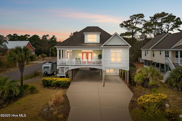 coastal home featuring a carport, concrete driveway, a porch, and a shingled roof