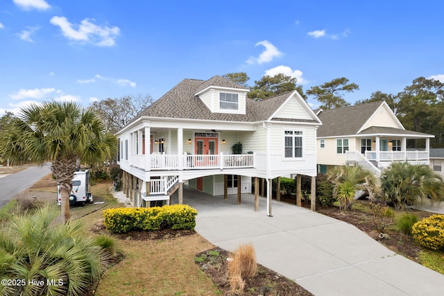 coastal inspired home with concrete driveway, roof with shingles, french doors, a porch, and a carport