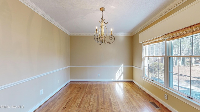 spare room with crown molding, a chandelier, a textured ceiling, and light wood-type flooring