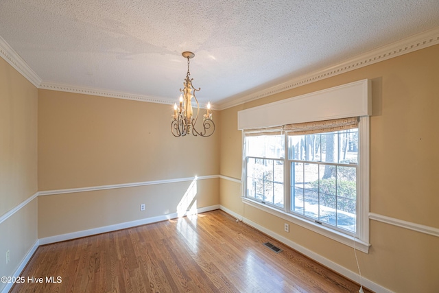 spare room featuring an inviting chandelier, hardwood / wood-style flooring, ornamental molding, and a textured ceiling