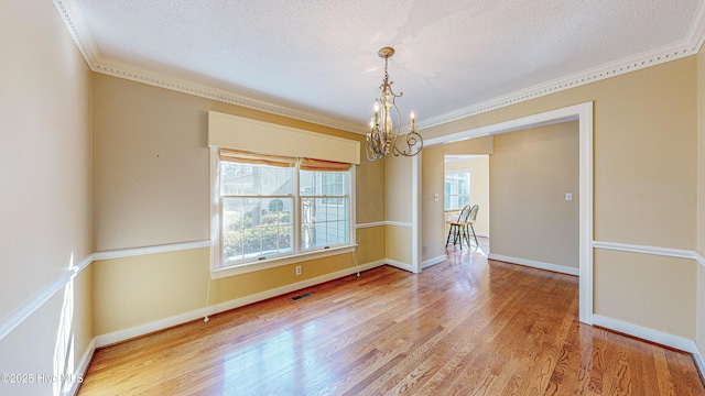 unfurnished dining area with ornamental molding, hardwood / wood-style floors, a notable chandelier, and a textured ceiling